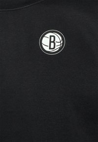 Suéter de algodón negro con un logo blanco redondo que muestra una "B" estilizada y líneas de baloncesto. Textura suave, cuello redondo, diseño minimalista.