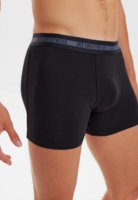 Černé boxerky s měkkým elastickým páskem, na kterém je logo "JBS UNDERWEAR". Hladká tkanina s přiléhavým střihem a délkou do poloviny stehna.