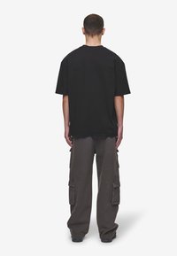 Black oversized t-shirt with short sleeves, paired with loose-fitting gray cargo pants featuring pockets and a cinched ankle design.