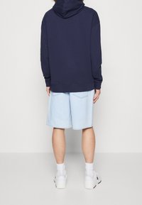 Navy blue hoodie with a drawstring and kangaroo pocket, paired with light blue denim shorts. White sneakers with contrasting accents.