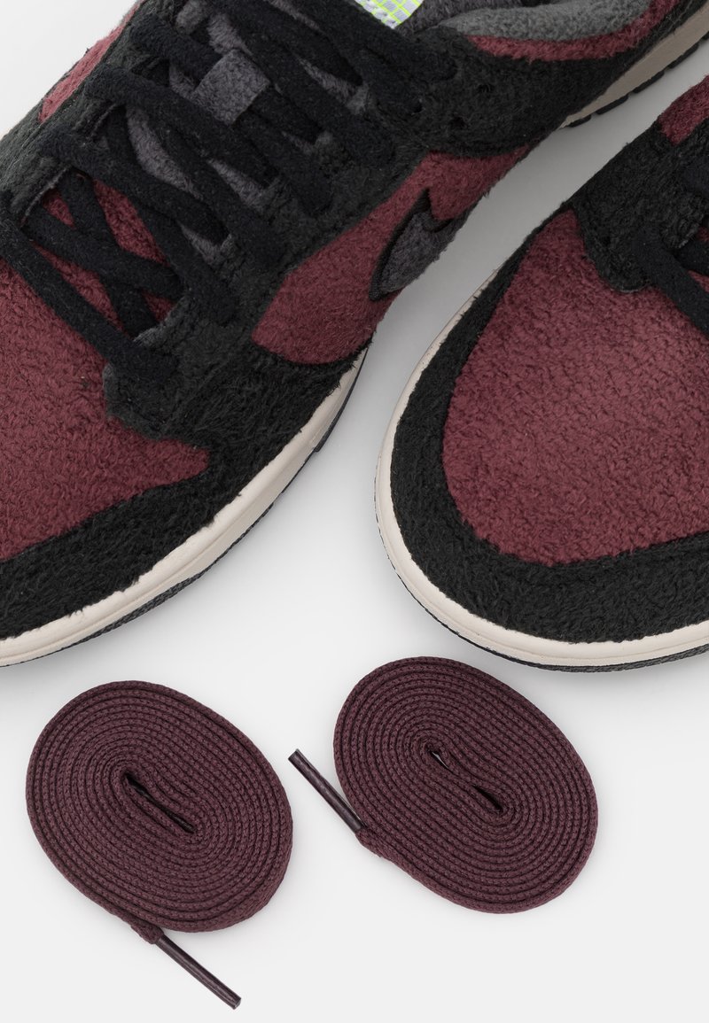 Sneaker mit schwarzem und burgunderfarbenem Textil-Obermaterial, mit strukturierter Oberfläche, schwarzen Schnürsenkeln und zwei zusätzlichen burgunderfarbenen Schnürsenkel-Optionen.