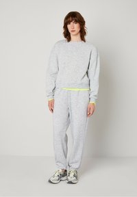 Light gray sweatshirt and sweatpants set made of soft fleece with a relaxed fit. Features neon accents at the hem and cuffs. Paired with running shoes.