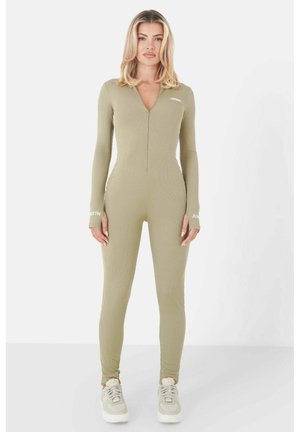 Olive green ribbed jumpsuit with long sleeves, zippered front, thumbhole accents, and branding on the sleeves. Paired with light sneakers.