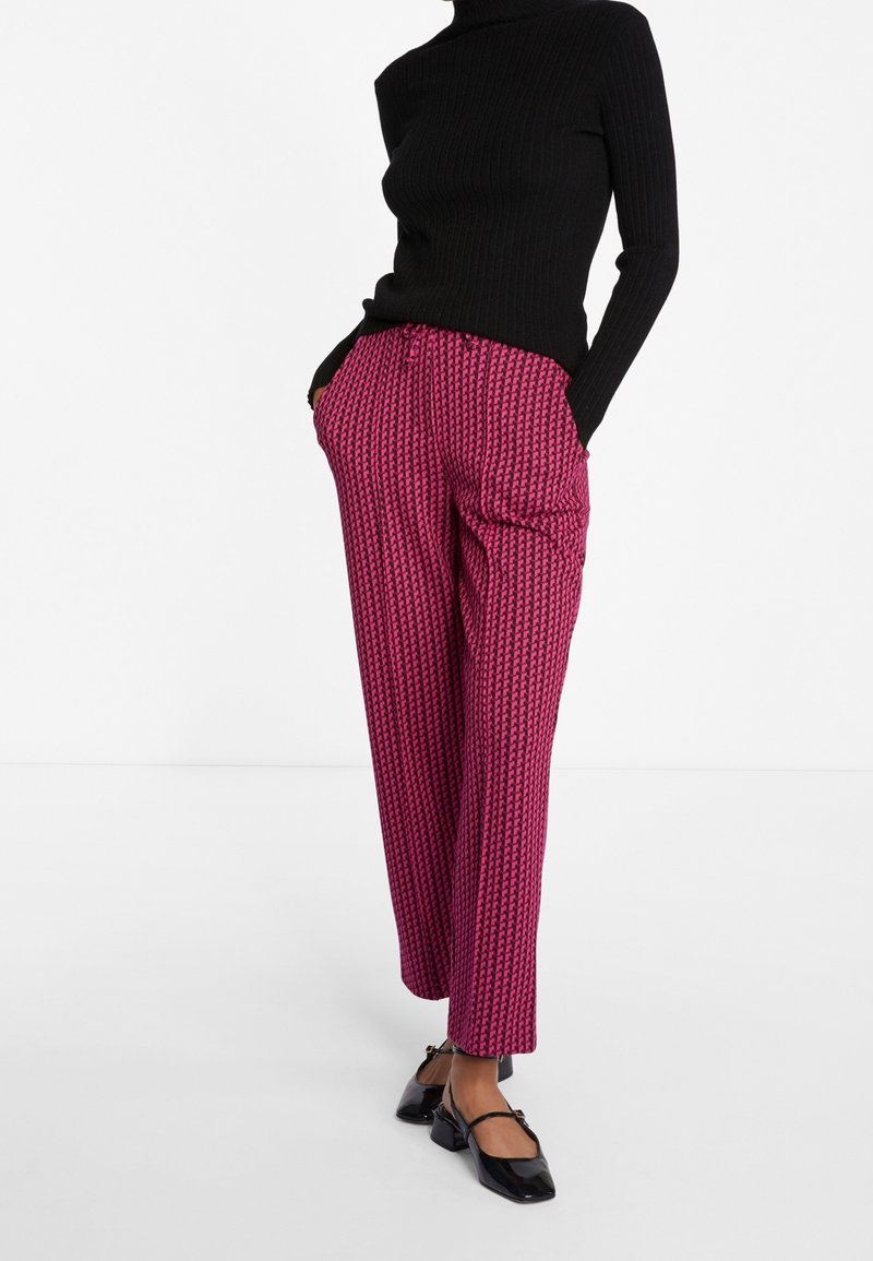 Schwarz eng anliegender gerippter Rollkragenpullover, kombiniert mit weit geschnittenen, rosa gemusterten Hosen mit geometrischem Design und Seitentaschen. Schwarze Ballerinas.