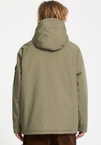 Veste vert olive avec capuche, dotée d'une texture lisse et de manches raglan. La vue montre les détails du dos, sans qu'aucune quincaillerie ou motif ne soit visible.