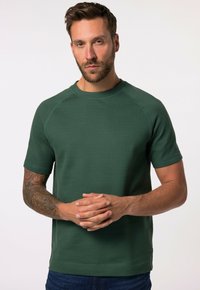 Sudadera de manga corta en verde con cuello redondo, confeccionada en un tejido texturizado. Incluye mangas raglán y detalles de costura en contraste.