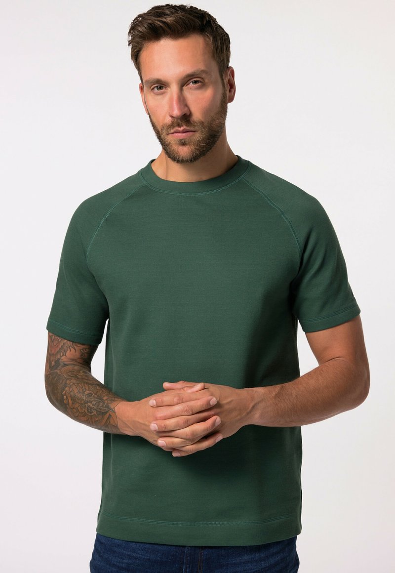 Sudadera de manga corta en verde con cuello redondo, confeccionada en un tejido texturizado. Incluye mangas raglán y detalles de costura en contraste.