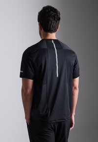 Zwart sportshirt met korte mouwen, voorzien van een verticale witte streep op de achterkant en gestructureerde panelen voor ventilatie.