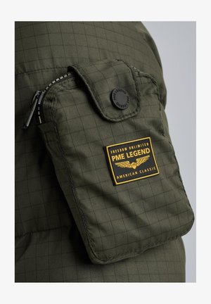 Olivgrüne gepolsterte Jacke mit einer Reißverschluss-Tasche und einem schwarzen Knopf sowie einem schwarzen und gelben Markenaufnäher mit geflügeltem Emblem.