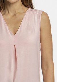 Blusa sin mangas de color rosa claro con escote en V y un pliegue central, hecha de una tela suave y ligeramente brillante.