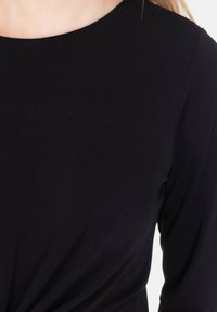 Top nero a maniche lunghe con scollo rotondo e tessuto morbido e strutturato. Presenta un dettaglio annodato in vita per un tocco di design in più.