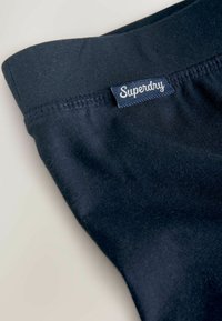 Tmavomodrý bavlnený pás s prešitím a modrou nálepkou s bielym textom. Mäkká textúra, bez vzorov alebo akcentov.