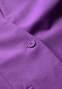Violet lino audinys su lygiu paviršiumi, turi apvalų mygtuką su keturiomis skylutėmis, pritvirtintą arti siūlės.