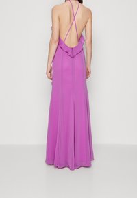 Long, backless dress in vibrant purple. Features thin crisscross straps and a ruffled accent along the neckline. Flowing, soft fabric.