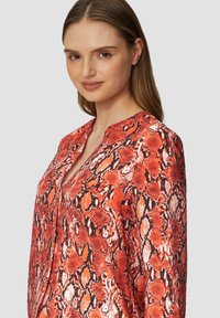 Bluse mit rotem und schwarzem Schlangenprint, V-Ausschnitt, langen Ärmeln und glattem, leichtem Stoff. Verfügt über einen subtilen Glanz und einen lockeren Schnitt.