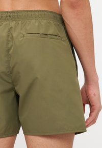 Zelené plavky z hladkej látky s elastickým pásom. Obsahujú zadnú vrecko a jednoduchý, čistý dizajn.
