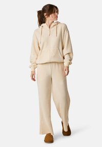 Felpa a coste color crema con zip frontale e tasche, abbinata a pantaloni a coste larghi coordinati e scarpe slip-on marroni.