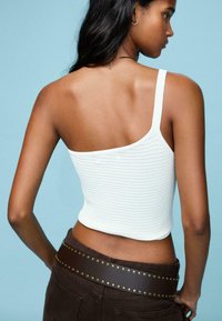 Weißes, geripptes Croptop mit einem breiten Träger, kombiniert mit dunkelbraunen Hosen und einem genietetem Ledergürtel. Strukturiertes Material.