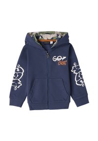 Sudadera de cremallera en color marino con capucha forrada en camuflaje. Presenta texto en estilo graffiti blanco y dos bolsillos frontales. Fabricada en una suave mezcla de algodón.