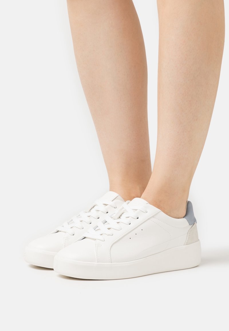 Baskets en cuir blanc à texture lisse, avec des accents gris sur le talon et les œillets, bout rond et semelle en caoutchouc plate.