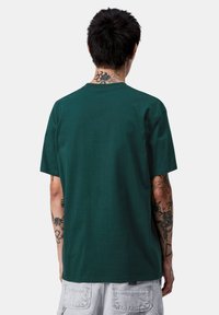 Camiseta de algodón verde con cuello redondo clásico y mangas cortas. Textura suave, ajuste relajado, sin marcas ni patrones visibles.