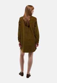 Robe en velours côtelé vert olive avec des manches longues, des poignets boutonnés et une coupe décontractée. Présente des fentes latérales près de l'ourlet et un empiècement au dos.