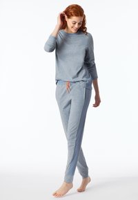 Conjunto de loungewear en gris claro que incluye una camiseta de manga larga y pantalones ajustados. Los pantalones tienen un cordón de ajuste naranja y detalles en canalé en los lados. Textura suave.