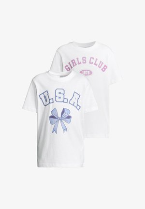 Witte t-shirt met de tekst "GIRLS CLUB 1976" in paars; gecombineerd met zwarte legging met multiculturele bloemmotieven; witte schoenen.