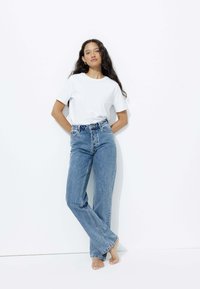 T-shirt en coton blanc associé à un jean flare taille haute bleu clair, avec des coutures détaillées et un design à cinq poches.