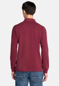 Bordová polokošile s dlouhým rukávem, límečkem a měkkou texturou, spárovaná s modrými džínami s zadními kapsami.