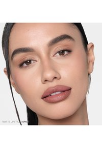Matte Lippenstift in einem warmen Gewürzton auf den Lippen. Glatte Textur mit mattem Finish. Subtile Augen-Make-up und ein sanfter Teint.