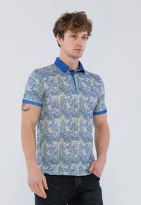 Polo de manga corta con un patrón texturizado en azul y verde, cuello y puños azules sólidos. Fabricado con un material liviano.