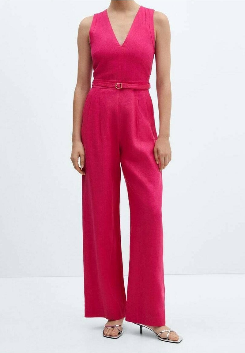 Femme portant une combinaison fuchsia sans manches avec un décolleté en V, une taille ceinturée, des jambes larges et des sandales à talons hauts argentées à brides, debout sur un fond blanc.
