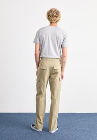 Beige cargobyxor med flera sidofickor, kombinerat med en grå t-shirt. Utstyrslen har en avslappnad passform och en casual stil.
