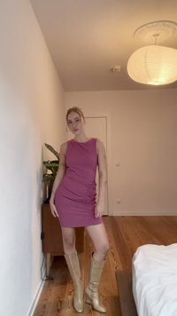 Figurbetontes rotes Kleid mit asymmetrischem Halsausschnitt und gerafftem Seitendetail. Zu kniehohen beigen Stiefeln in einer neutralen Umgebung getragen.