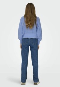 Overdimensjonert lyseblå strikkegenser med ribbestrikkede mansjetter, parret med høyhalsede blå denim flared jeans, sett fra baksiden.