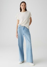 Lichtgewicht, crème ribgebreid t-shirt met korte mouwen, gecombineerd met high-waisted, lichtblauwe wijde jeans met een trekkoord in de taille.