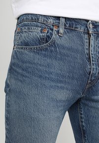 Jeans i ljusblå denim med texturerad yta. Har fem fickor, kopparnitar och dragkedjeförslutning. Klassisk rak bensnitt.