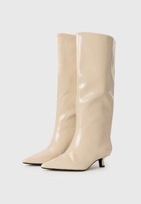 Beige knee-high boots made of glossy material, featuring a pointed toe and a small, tapered heel. Smooth texture and minimal design.