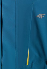 Tissu bleu avec une petite section jaune visible en dessous, comportant un logo "4F" argenté en haut à droite.