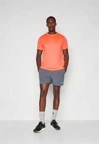 Conjunto deportivo masculino que incluye una camiseta de manga corta de color naranja brillante y pantalones cortos grises. Se lleva con zapatos negros y calcetines grises.
