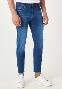 Jeans in denim blu con una vestibilità slim, texture sbiadita, design a cinque tasche e una classica chiusura a zip. Abbinati a sneaker bianche.