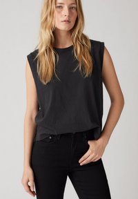 Top negro sin mangas hecho de una tela suave, con un corte relajado, cuello redondo y diseño minimalista, combinado con jeans negros.