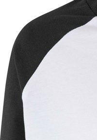 Fekete-fehér pamut póló, fekete raglán ujjal és fehér testtel. Simított textúra, szabványos kerek nyakkivágással.