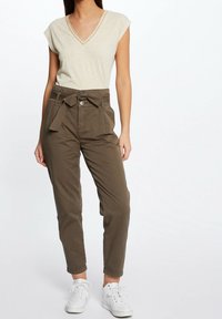 Beige V-neck shirt with short sleeves; olive green trousers with a tie belt and front pockets; worn with white sneakers.