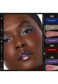 Primo piano di un volto di pelle scura con un eyeliner blu audace, ombretto viola scintillante, labbra metalliche viola e diversi campioni di colori di trucco etichettati nelle vicinanze.