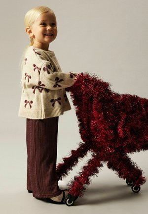 Gebreid crèmekleurig sweater met maroon strikpatronen; maroon textuurbroek; rode speelgoedkar met glinsterende effecten, voorzien van vier wielen en een fluffy textuur.