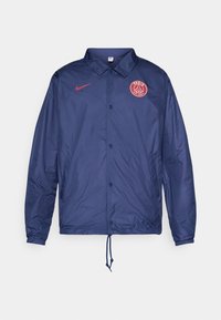 Navy blue Nike jacket with snap buttons, Paris Saint-Germain logo on chest, elastic cuffs, and drawstring hem.