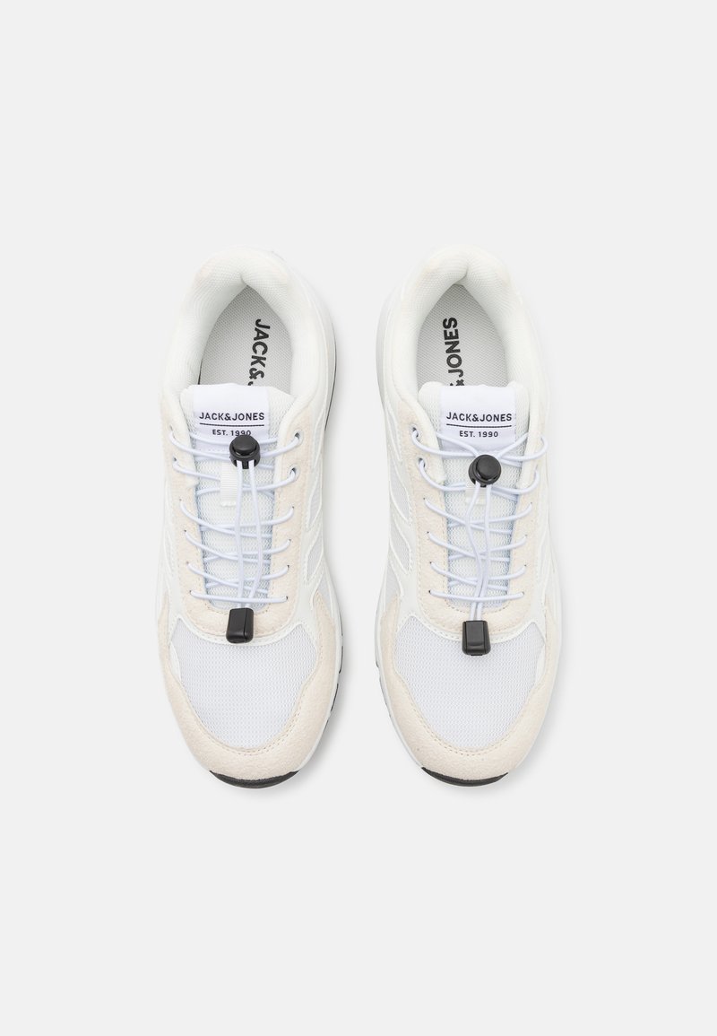 Zapatillas blancas con materiales de malla y gamuza, con un diseño sin cordones, un regulador ajustable y detalles en negro en la suela y en los cordones.