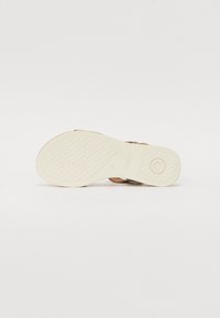 Tan leather sandal with a textured white rubber sole. Features an adjustable buckle and a rounded toe design. Brand logo visible on the sole.